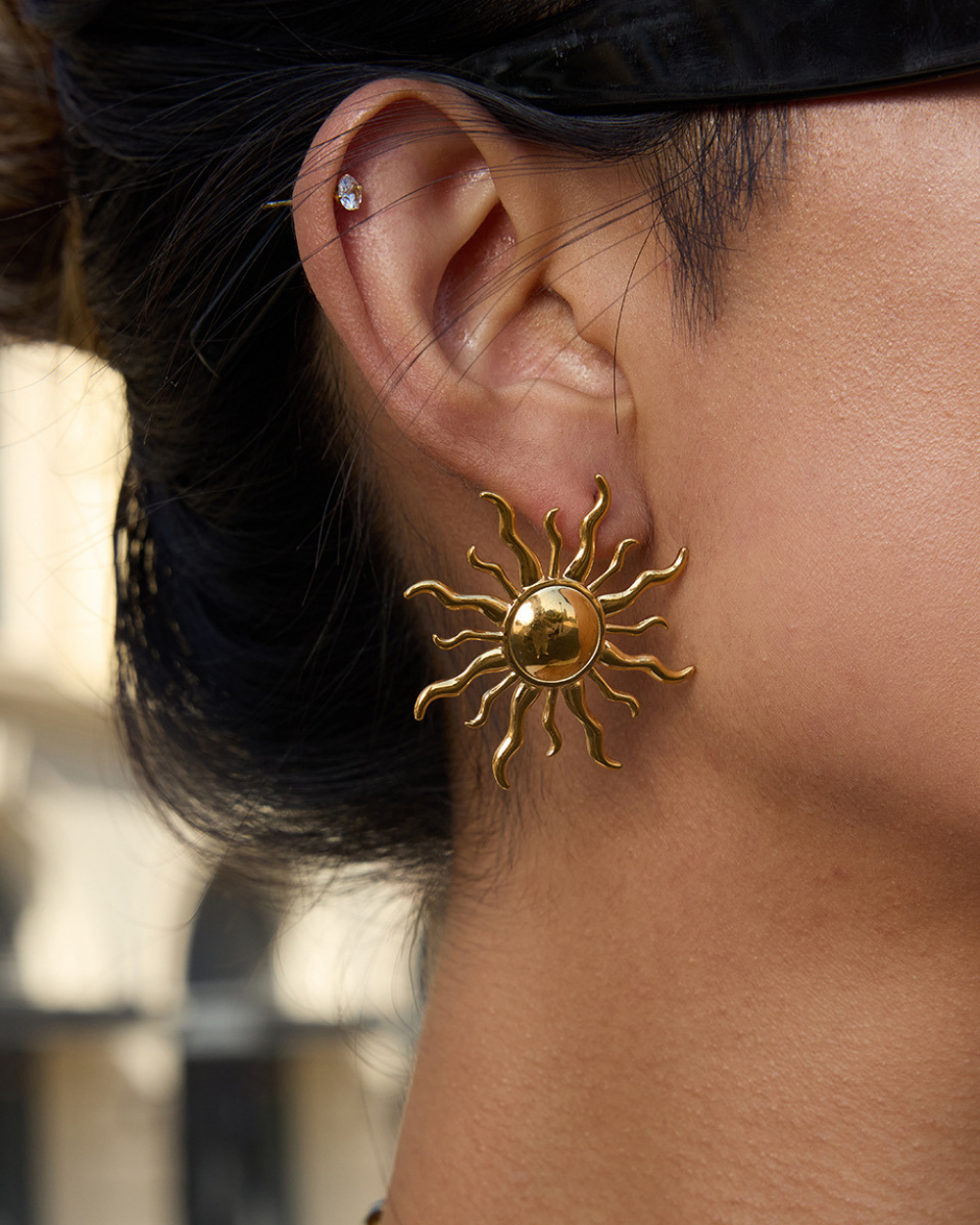 Gold sun-shaped earring worn by a person with a blurred background