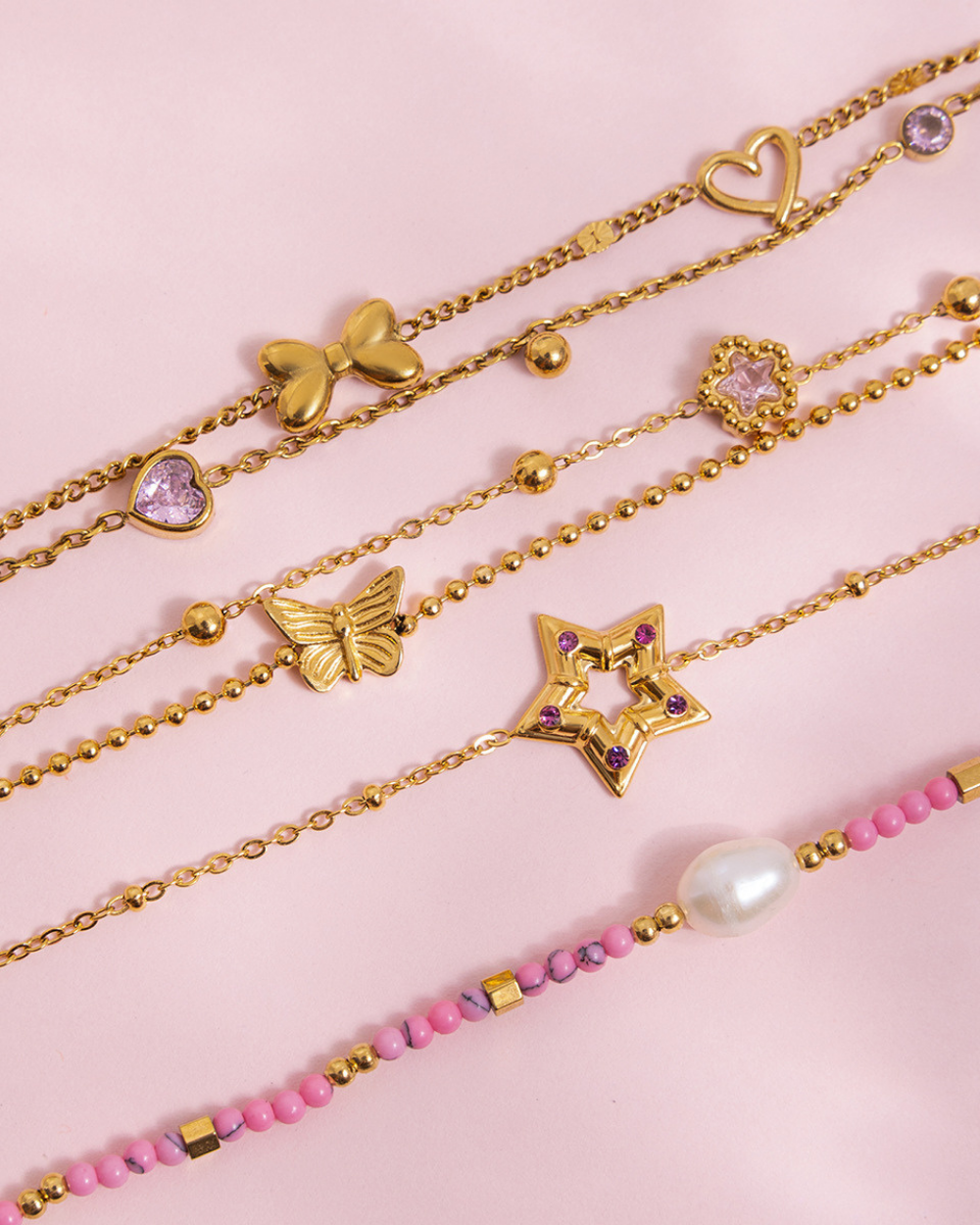 Set of gold and pink beaded bracelets on a pink background