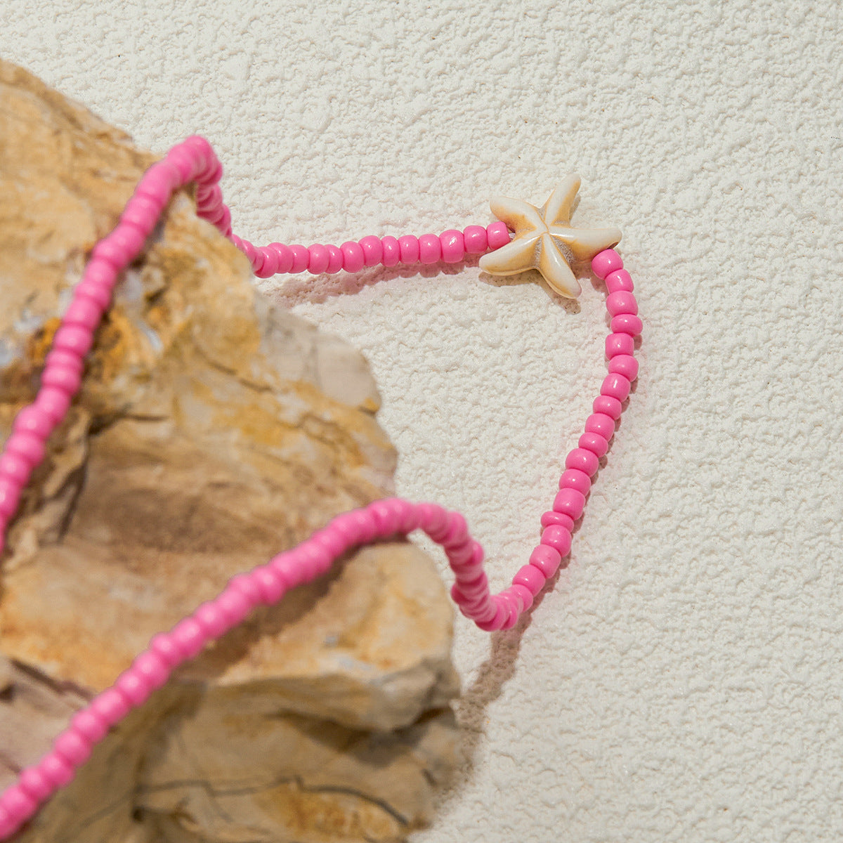 Pink starfish necklace styled on a tray next to beach-themed decor, showing waterproof and non-fade quality.