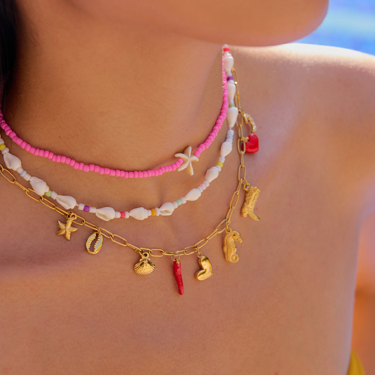 Female model wearing pink starfish necklace at the beach, styled with swimwear and summer glow.