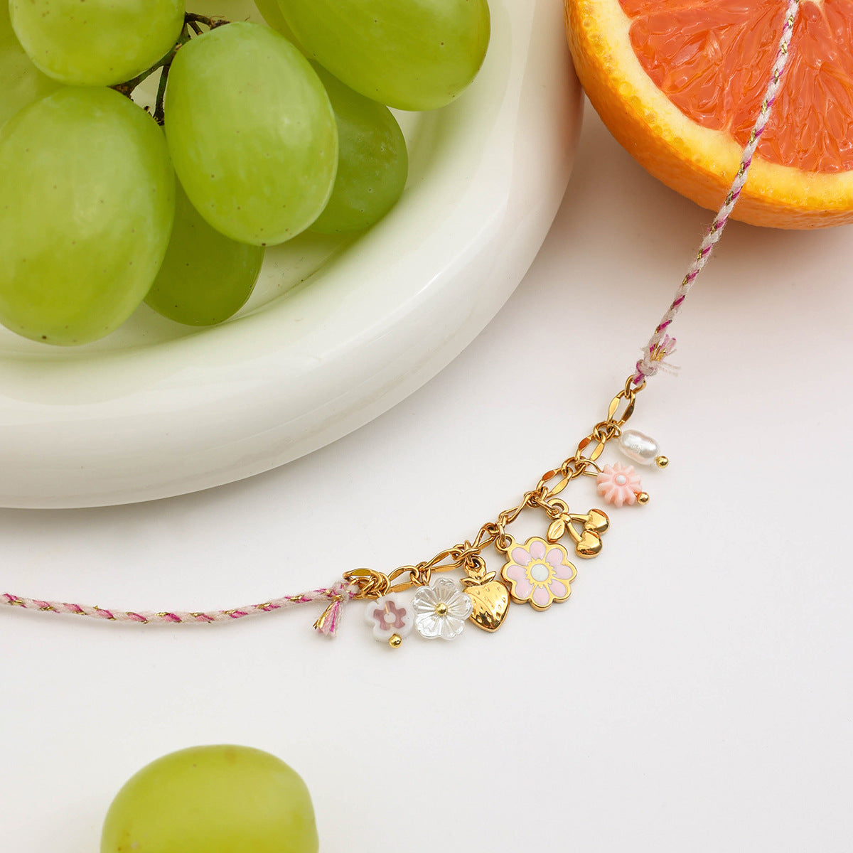Gold flower and heart charm necklace with pink cord on fruit background