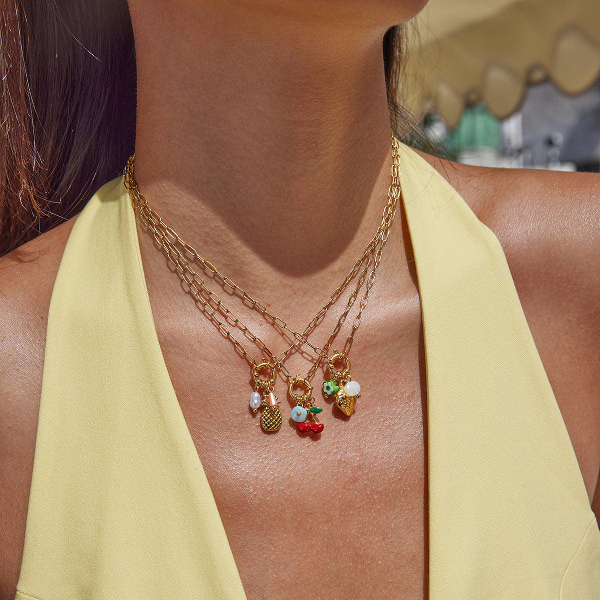 Close-up of a person wearing a gold necklace with colorful charms against a blurred background.