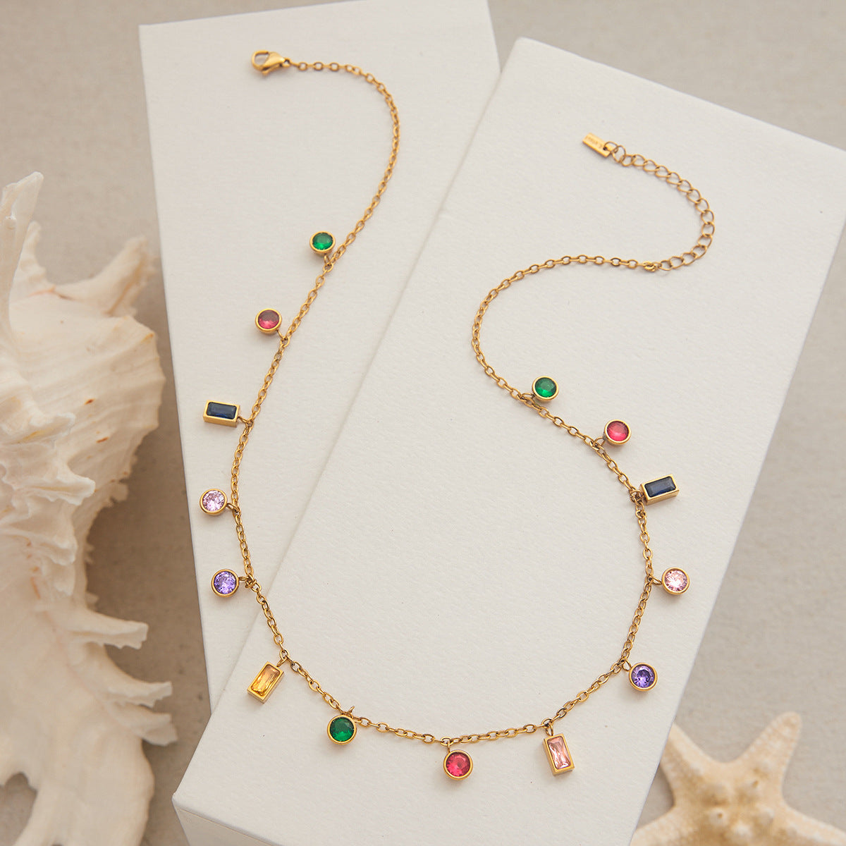 Gold chain necklace with rainbow gemstones styled on beige linen with seashells, beach theme