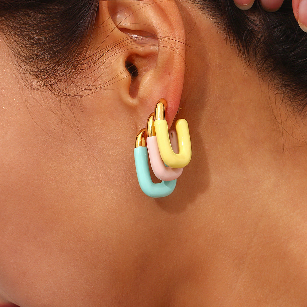Model wearing layered pastel enamel U hoop earrings in yellow, pink, and blue with gold caps