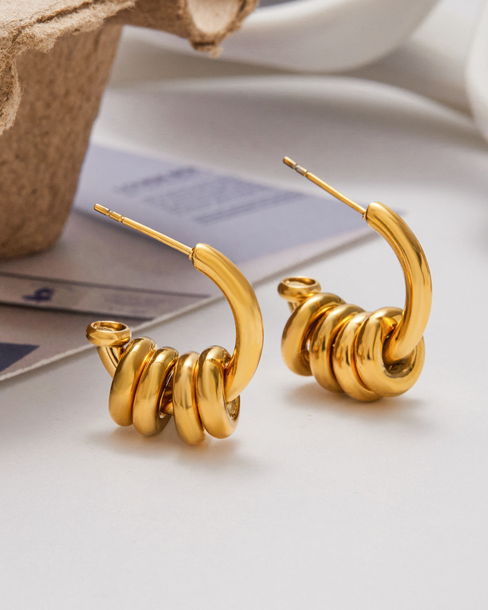 Gold spiral hoop earrings on a light surface with a blurred background