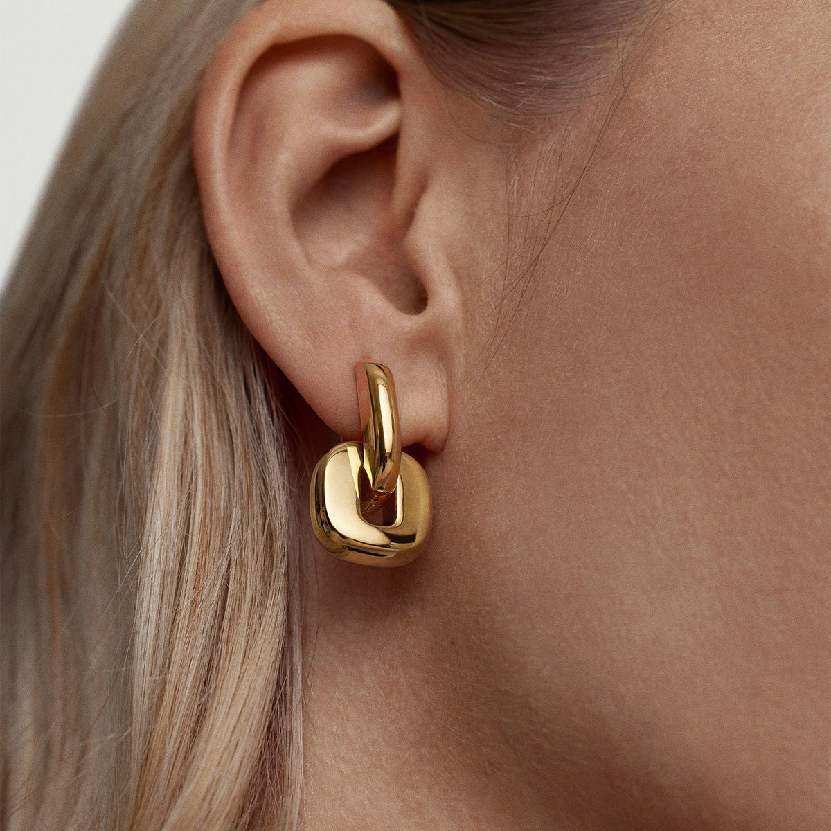 Female model wearing gold drop earrings, highlighting lobe and hair detail.