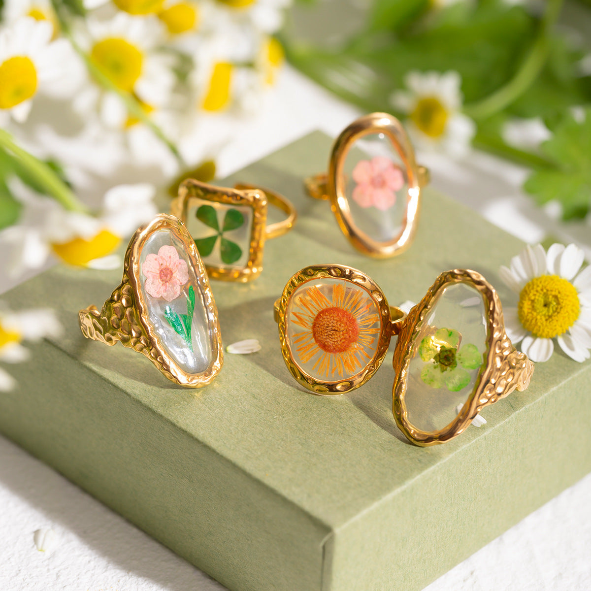 Group of flower-themed resin rings on floral box, sunlight filtering over petals