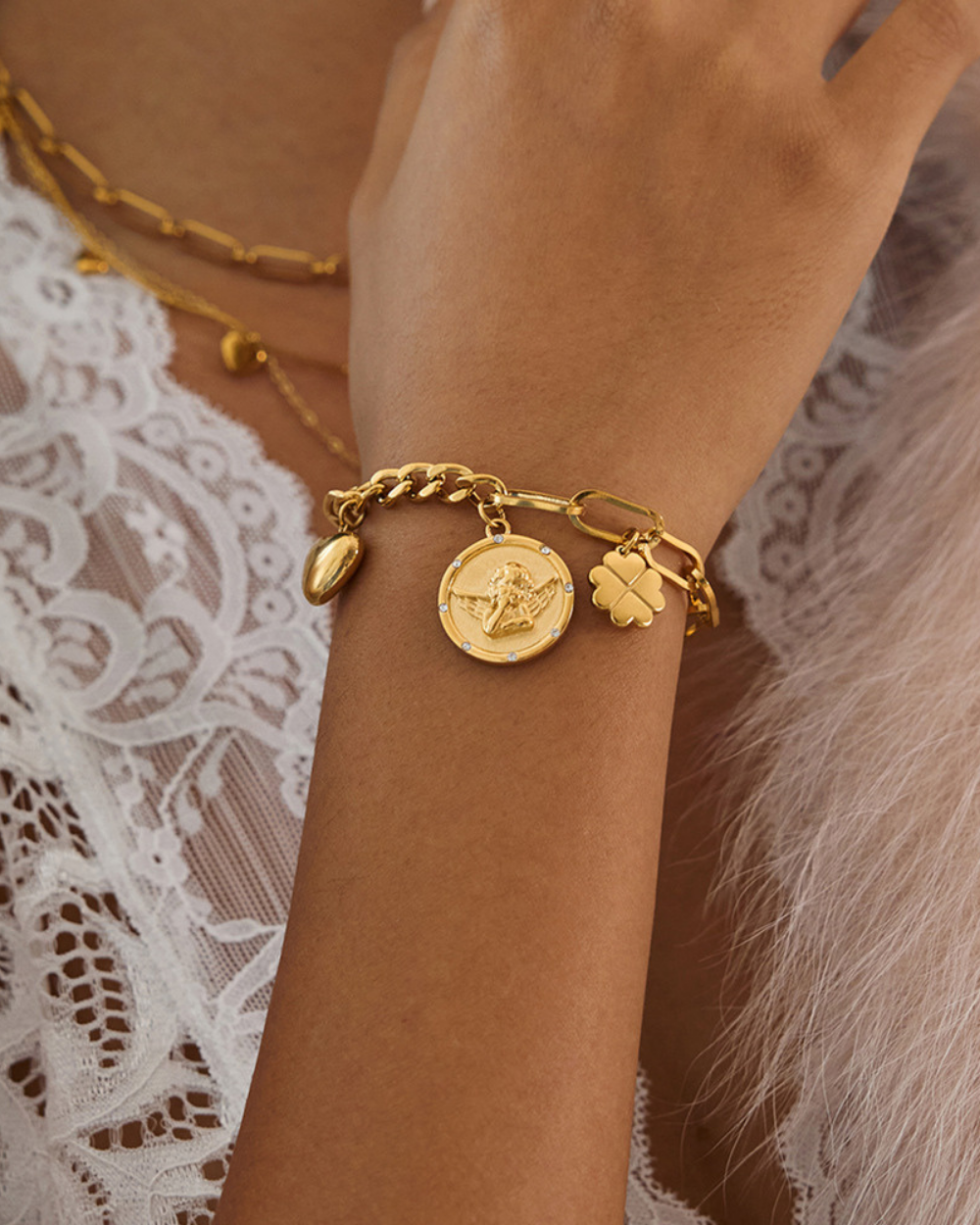 Gold bracelet with charms on a wrist against a lace fabric background