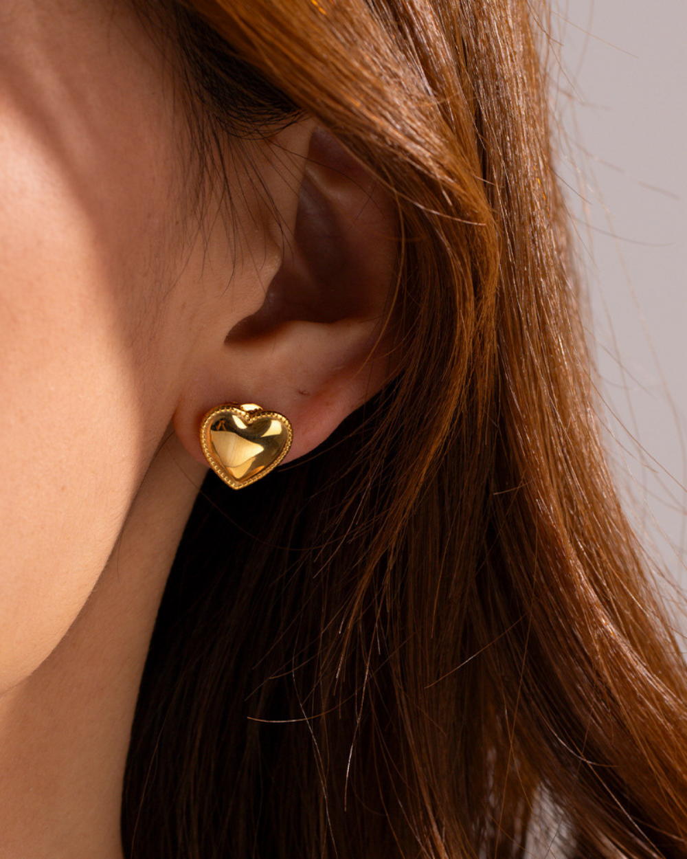 Gold heart-shaped earring worn by a person with brown hair.