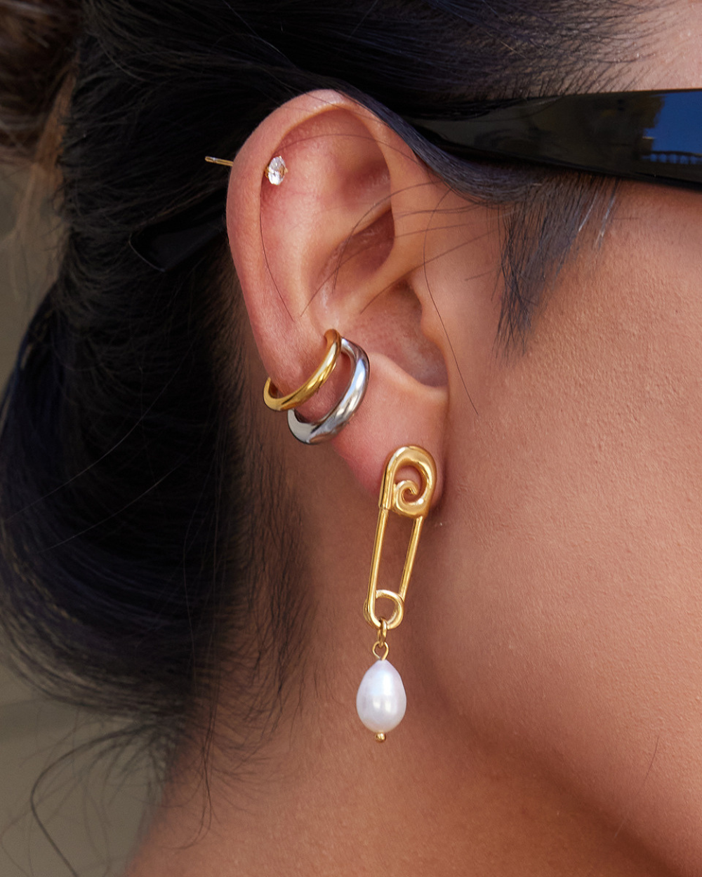 Close-up of an ear wearing a gold and silver hoop earring with a pearl drop earring.