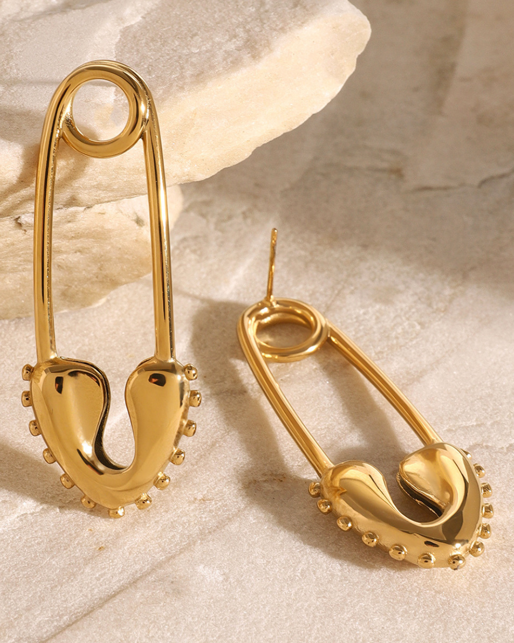 Gold safety pin earrings on a textured beige surface