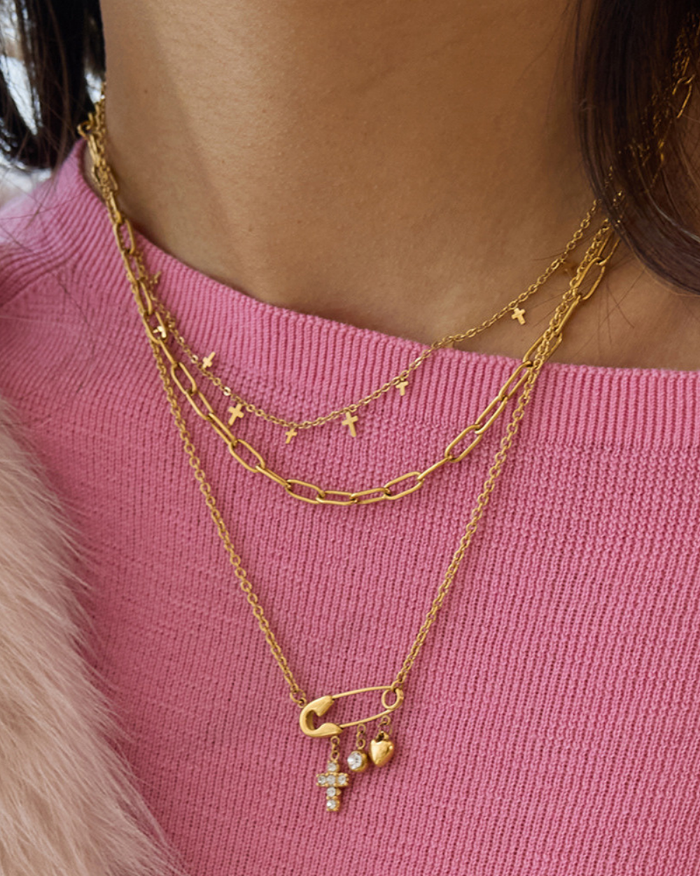 Gold necklaces with charms on a pink sweater