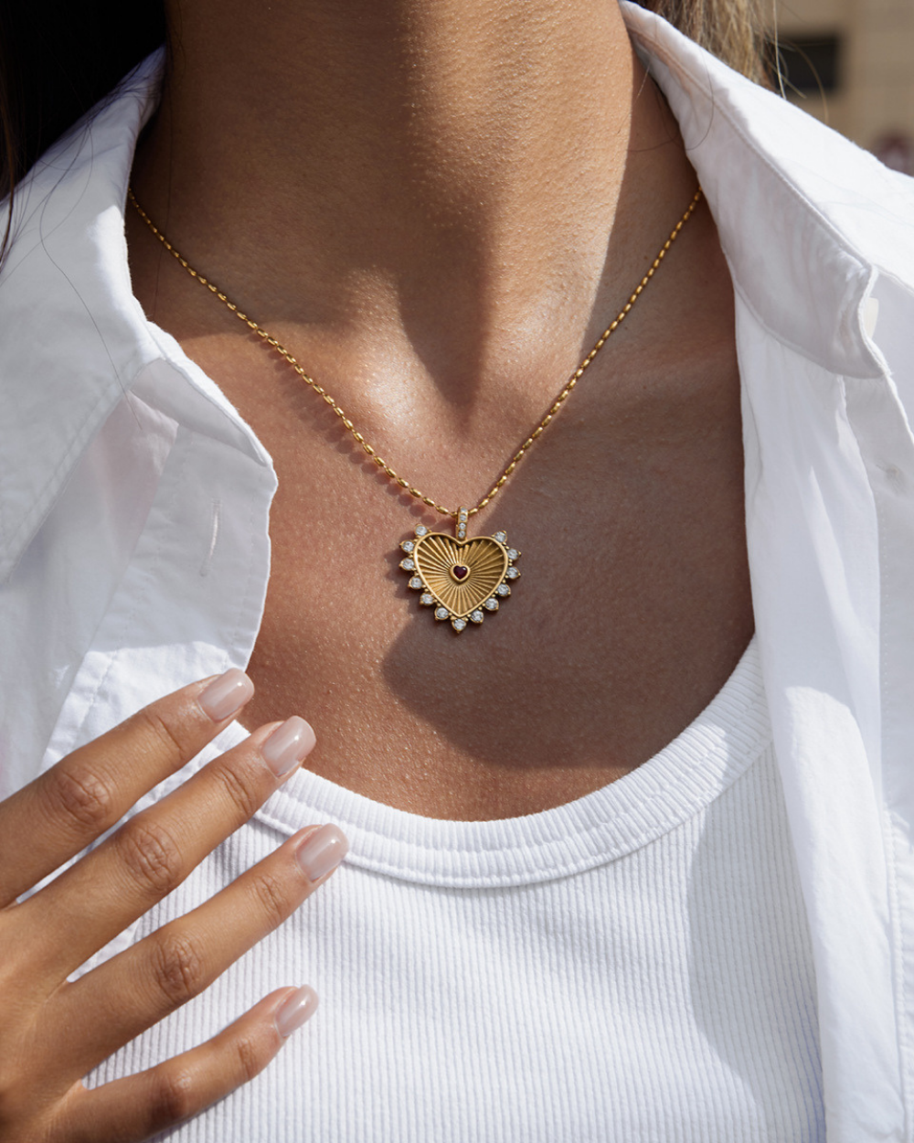 Gold heart-shaped necklace worn by a person in a white shirt.