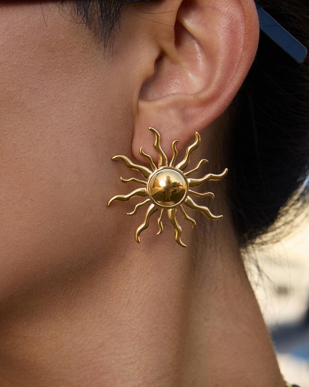 Gold sun-shaped earring worn by a person