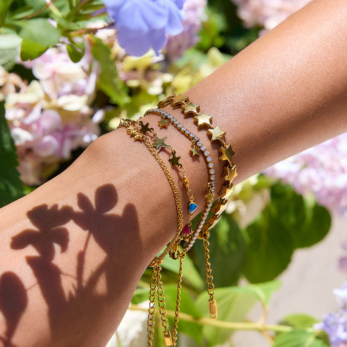 Model wearing layered gold bracelets with colorful heart and star charms