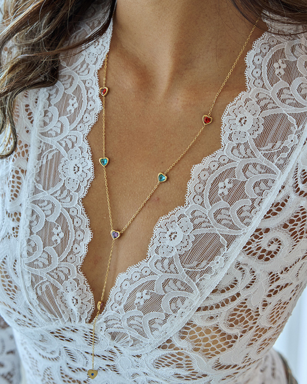 Close-up of a person wearing a gold necklace with colorful stones through a lace garment.