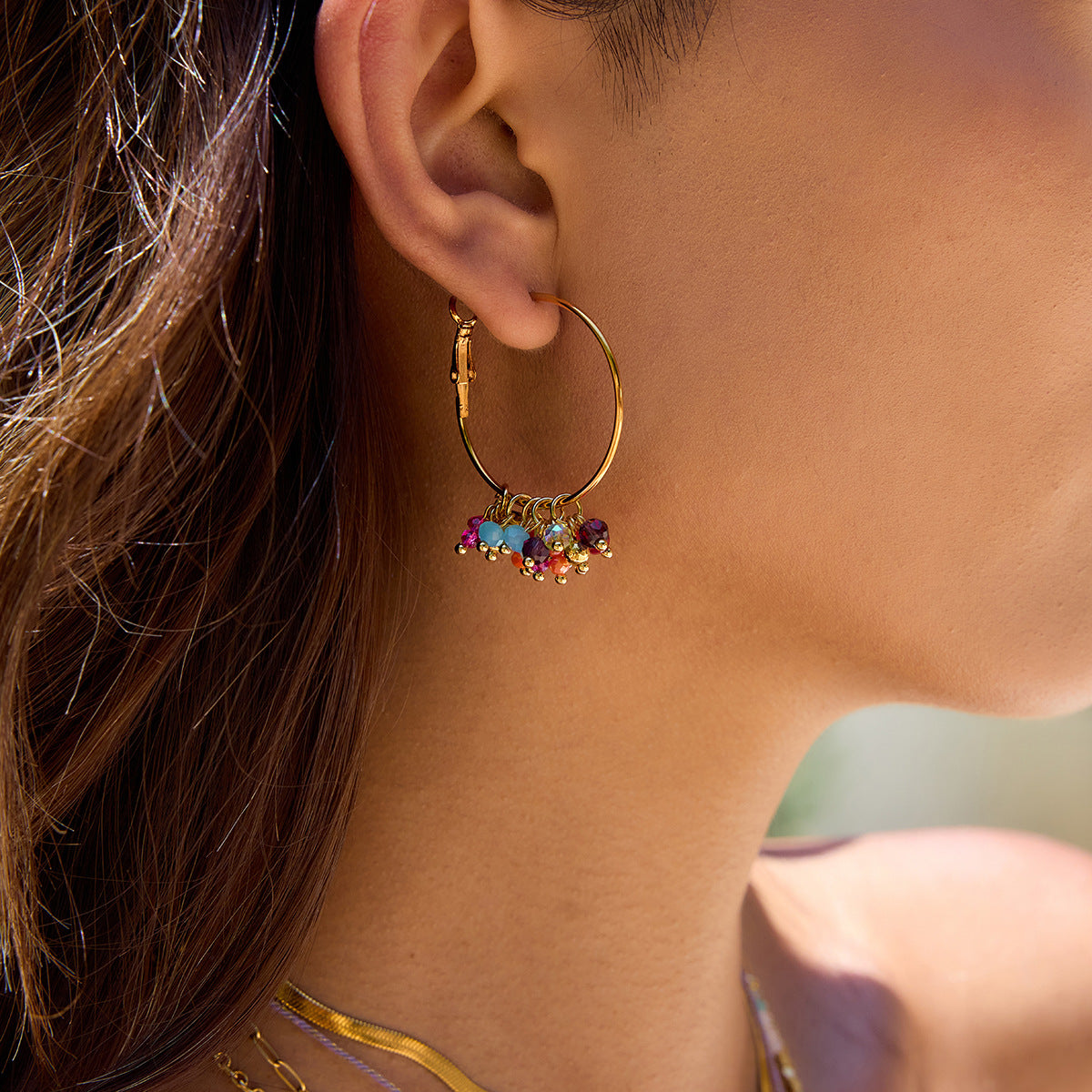 Close-up of an ear wearing a gold hoop earring with colorful beads.