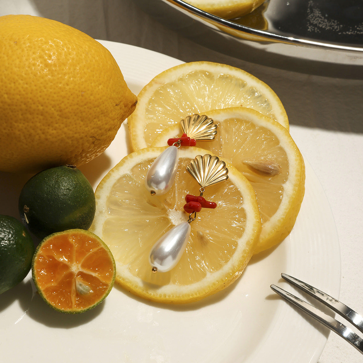 Statement earrings with coral branches and pearl drops placed with citrus fruits for summer vibe