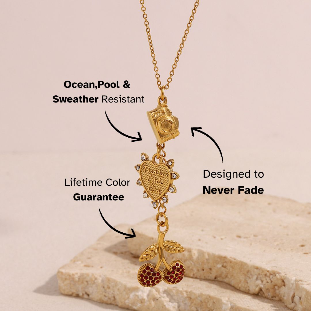 Vintage gold necklace with enamel cherry and camera charms, styled on beige stone, perfect for playful streetwear.