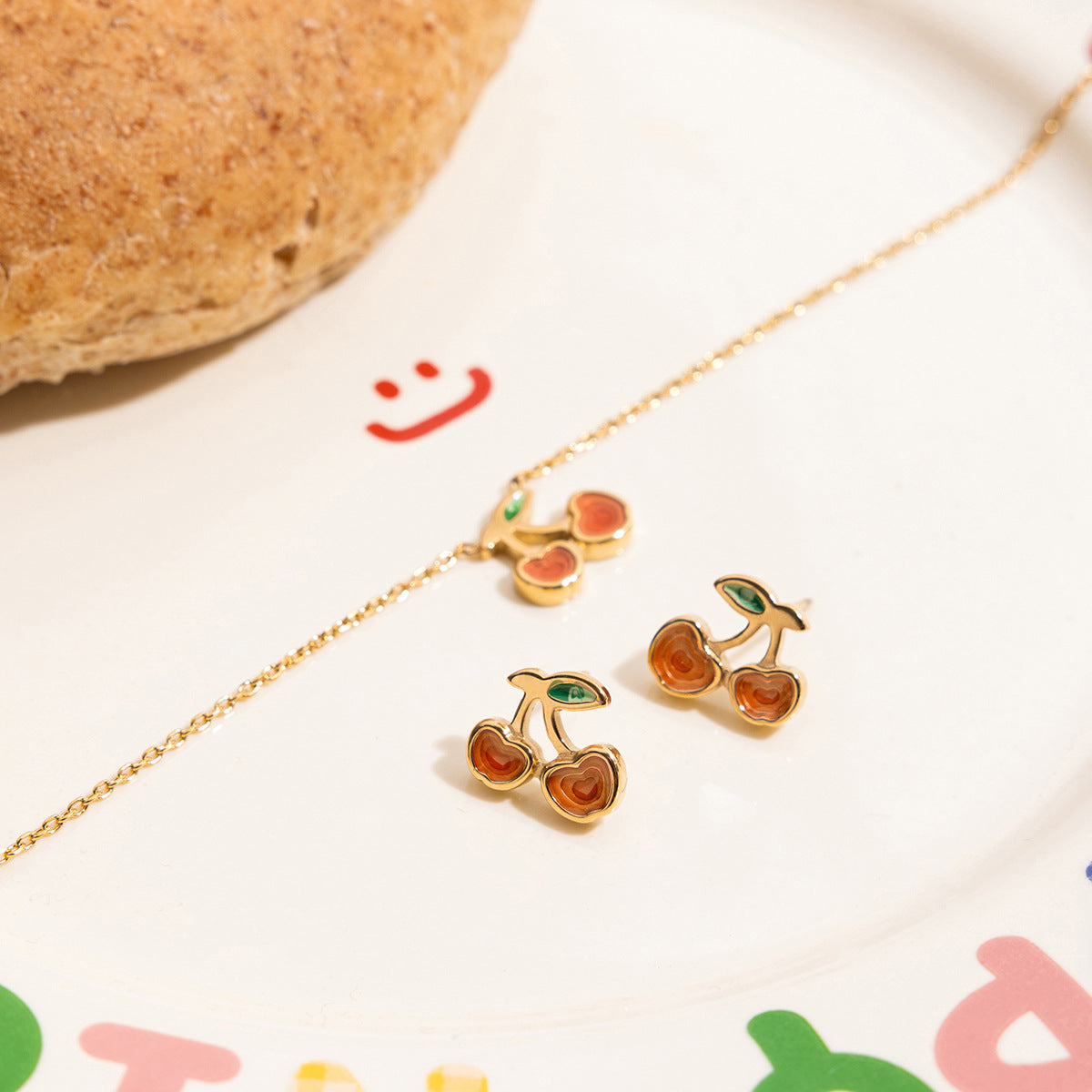 Gold cherry-shaped earrings on a white surface with colorful letters in the background