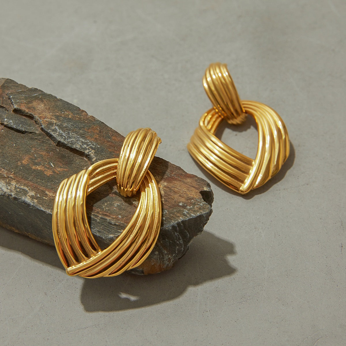Statement sculptural gold hoops with ribbed design on stone surface
