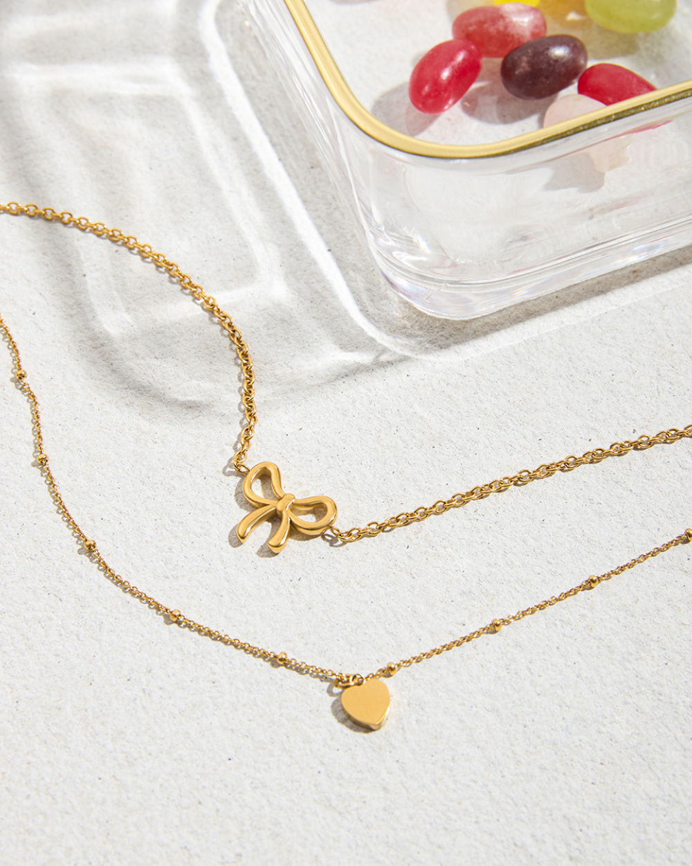 Gold necklace with bow and heart charms on a white fabric background