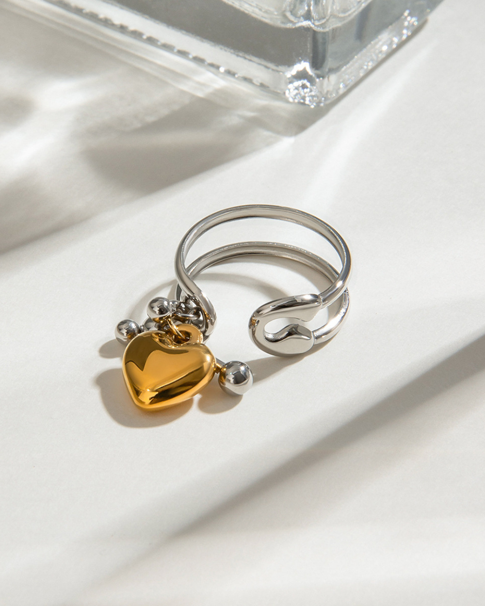 Silver ring with a gold heart charm on a white surface