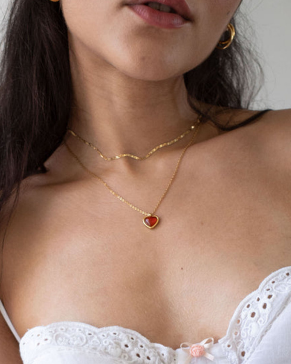 Close-up of a person wearing a gold necklace with a heart pendant.