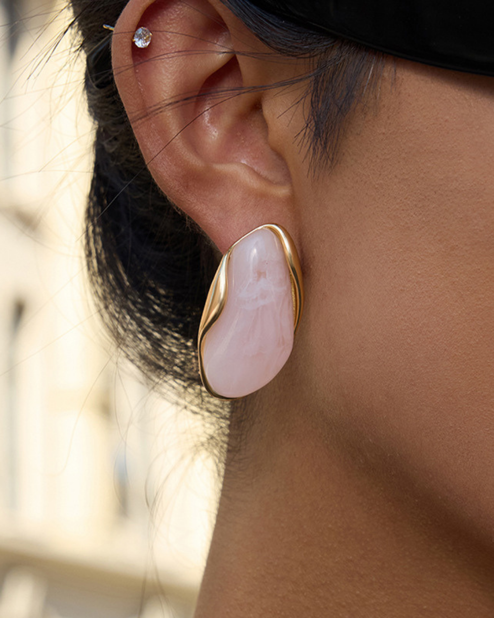 Close-up of an ear wearing a pink stone earring with gold setting.
