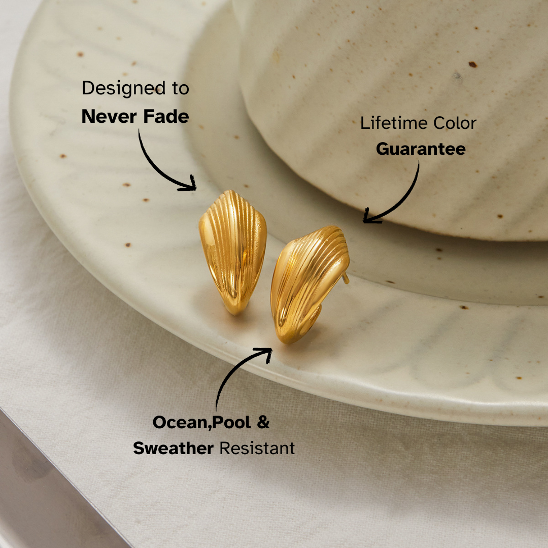 Minimal gold wave-shaped stud earrings on ceramic plate