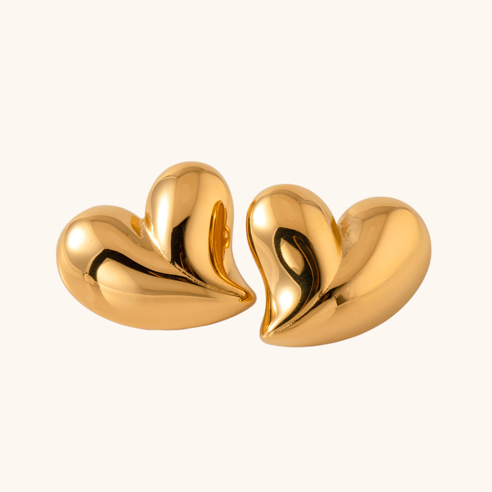 Polished gold-tone heart earrings with a sculpted puffed style on beige background