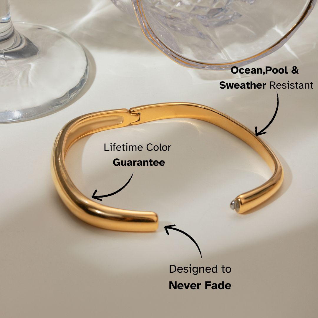 Polished gold-tone cuff bracelet next to glass — luxury waterproof jewelry with a modern clasp design