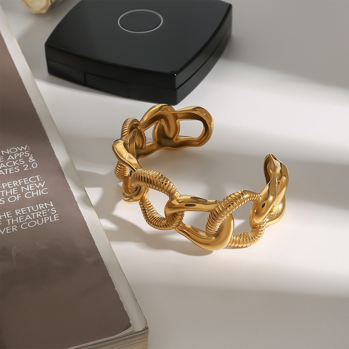 Statement gold bracelet with textured links, placed beside a compact case