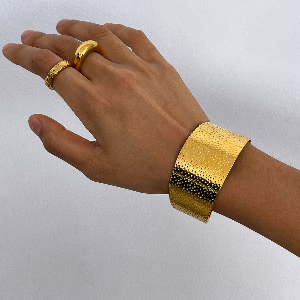 Hand wearing a gold bracelet and ring on a plain background