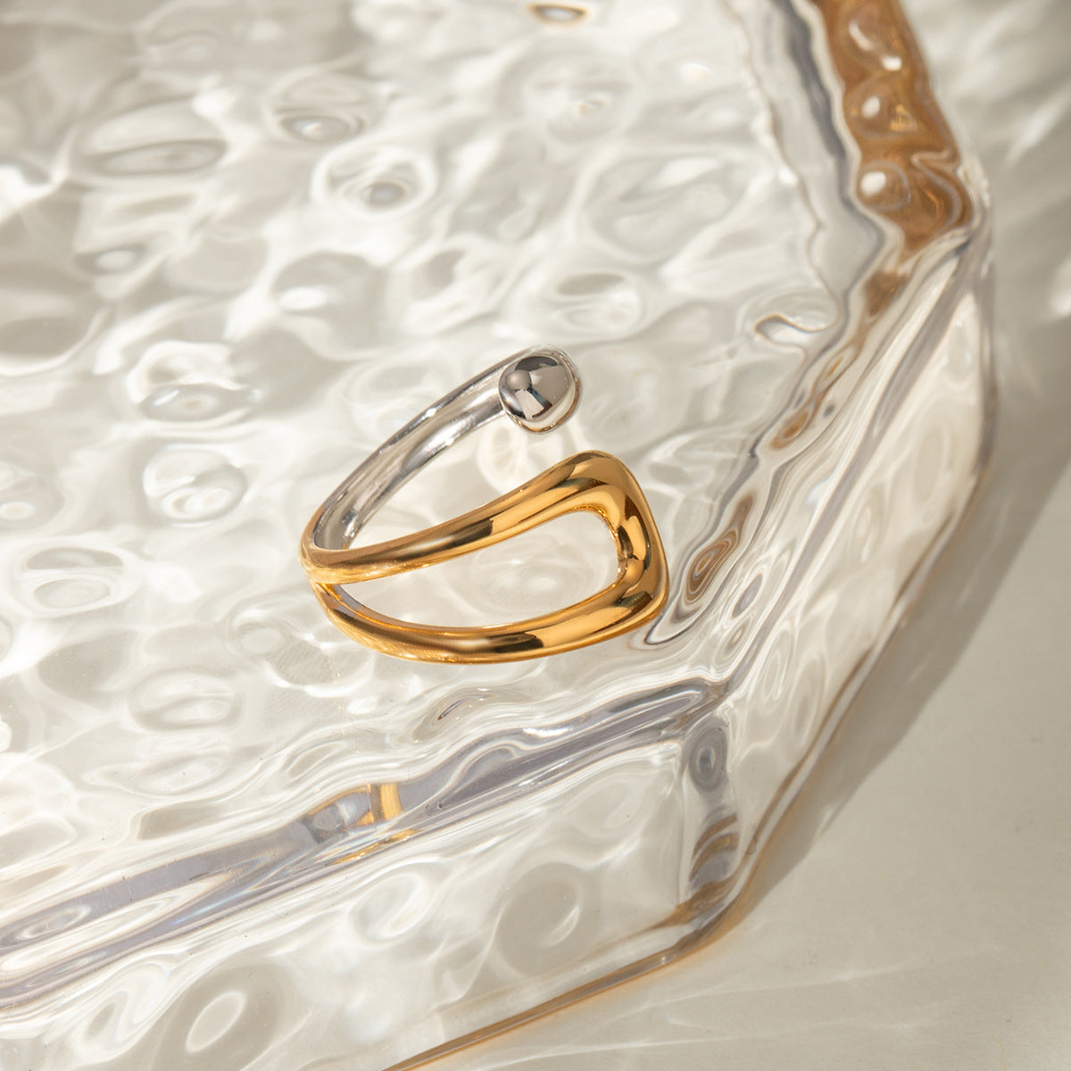 Two-tone adjustable ring placed on textured glass surface with elegant lighting.