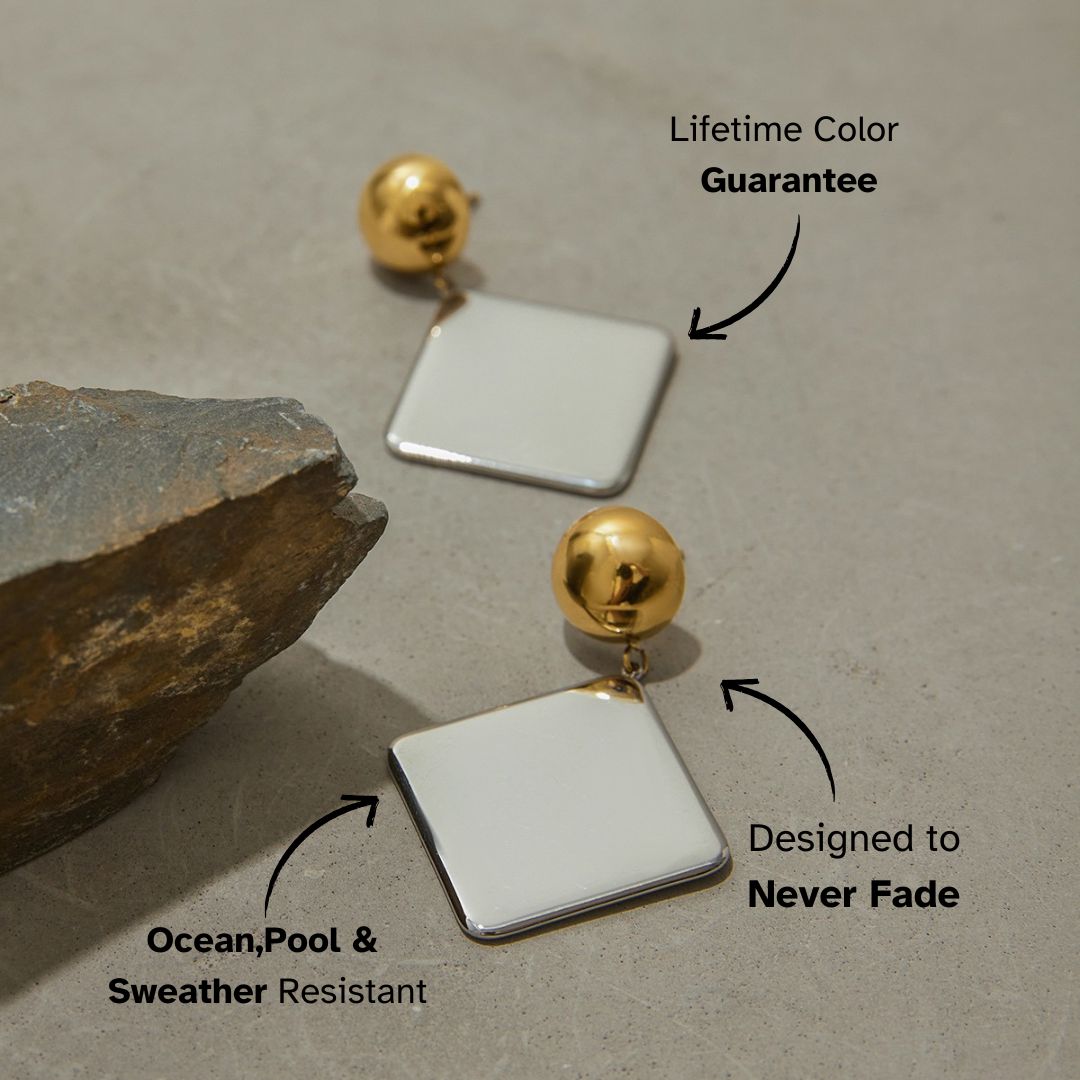 Minimalist metallic drop earrings laid on neutral concrete