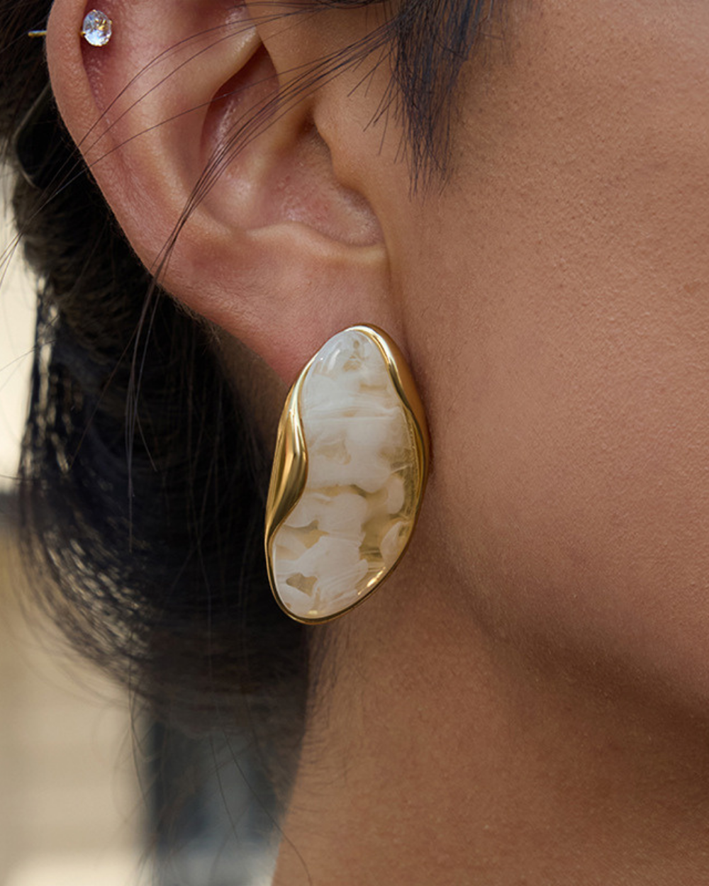 Close-up of an ear wearing a gold and beige earring with a blurred background