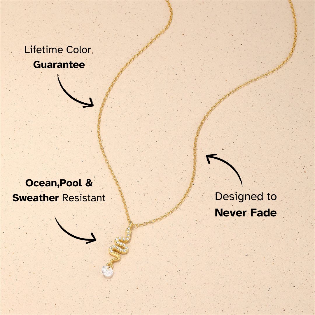 Snake pendant gold necklace with crystal drop, flat lay on creamy stone background
