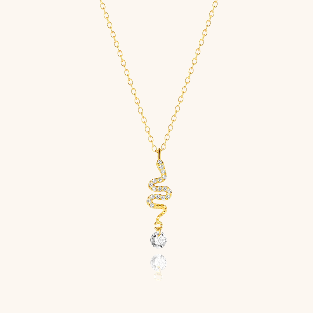 Gold twisted snake necklace with crystal drop laid on beige background, delicate and stylish