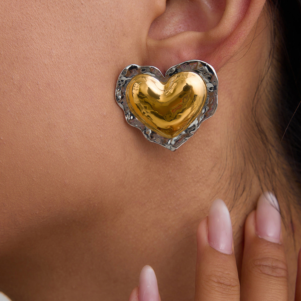 Gold heart earrings with silver hammered border on model’s ear