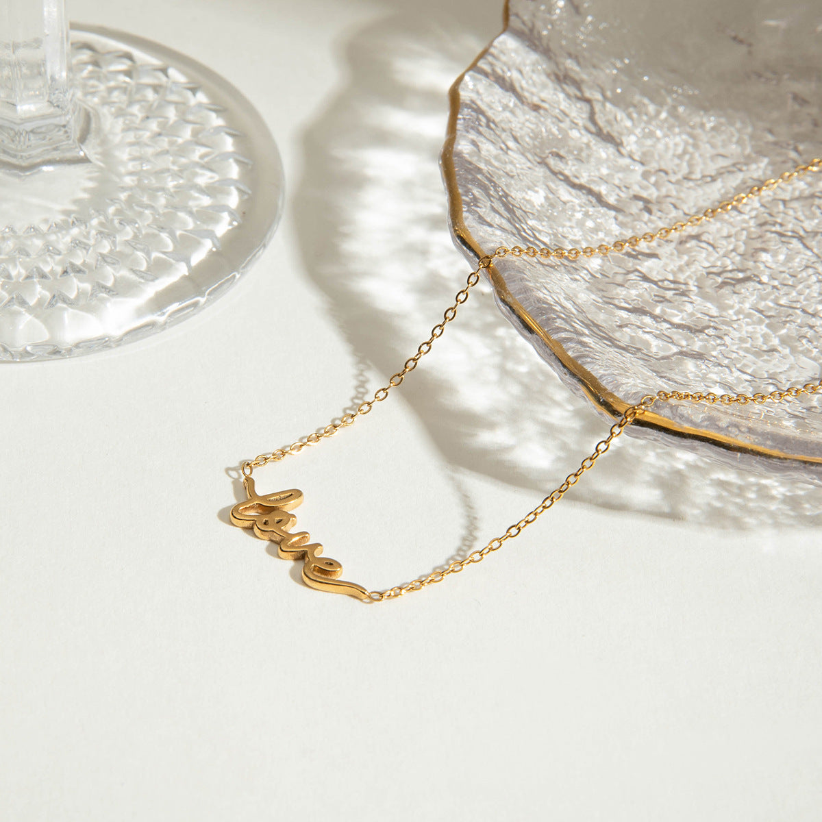 Lightweight gold "love" pendant necklace photographed near glass dish