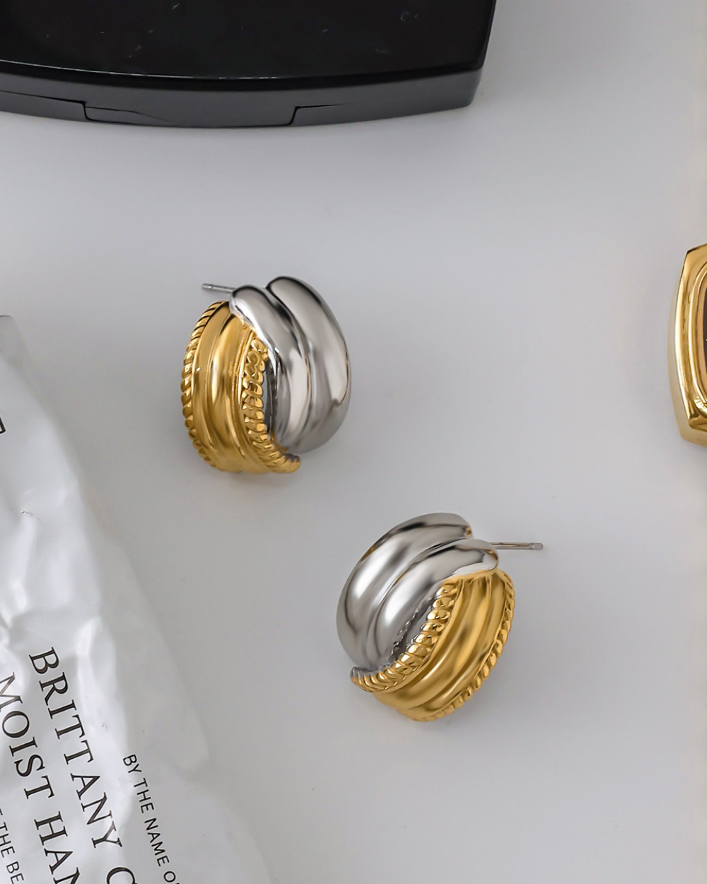 Gold and silver hoop earrings on a white surface with text in the background