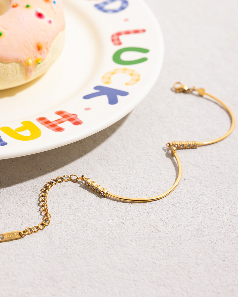 Gold bracelet on a light gray surface with a colorful alphabet plate in the background