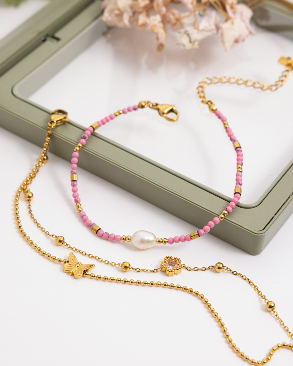 Gold and pink beaded bracelets on a white surface with a green jewelry box in the background.