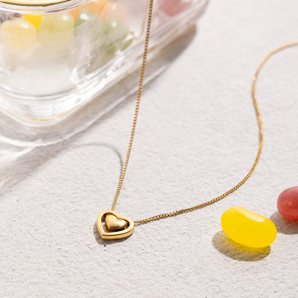 Gold heart-shaped necklace on a light surface with colorful jelly beans.