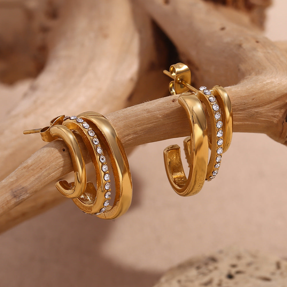 Gold hoop earrings with embedded stones on a wooden branch