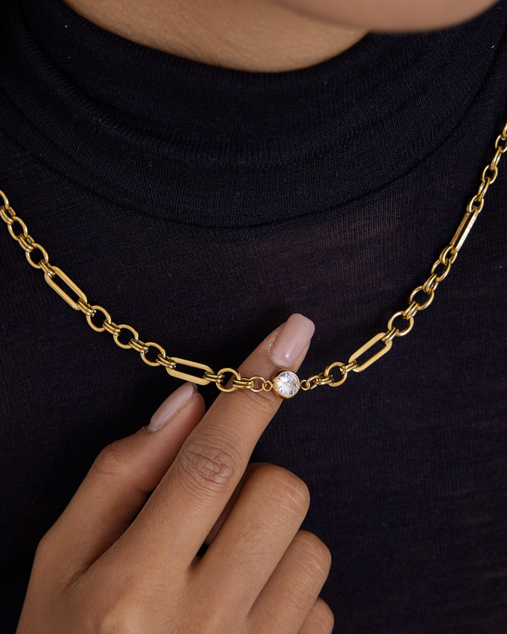 Gold chain necklace with a diamond pendant worn by a person on a black background