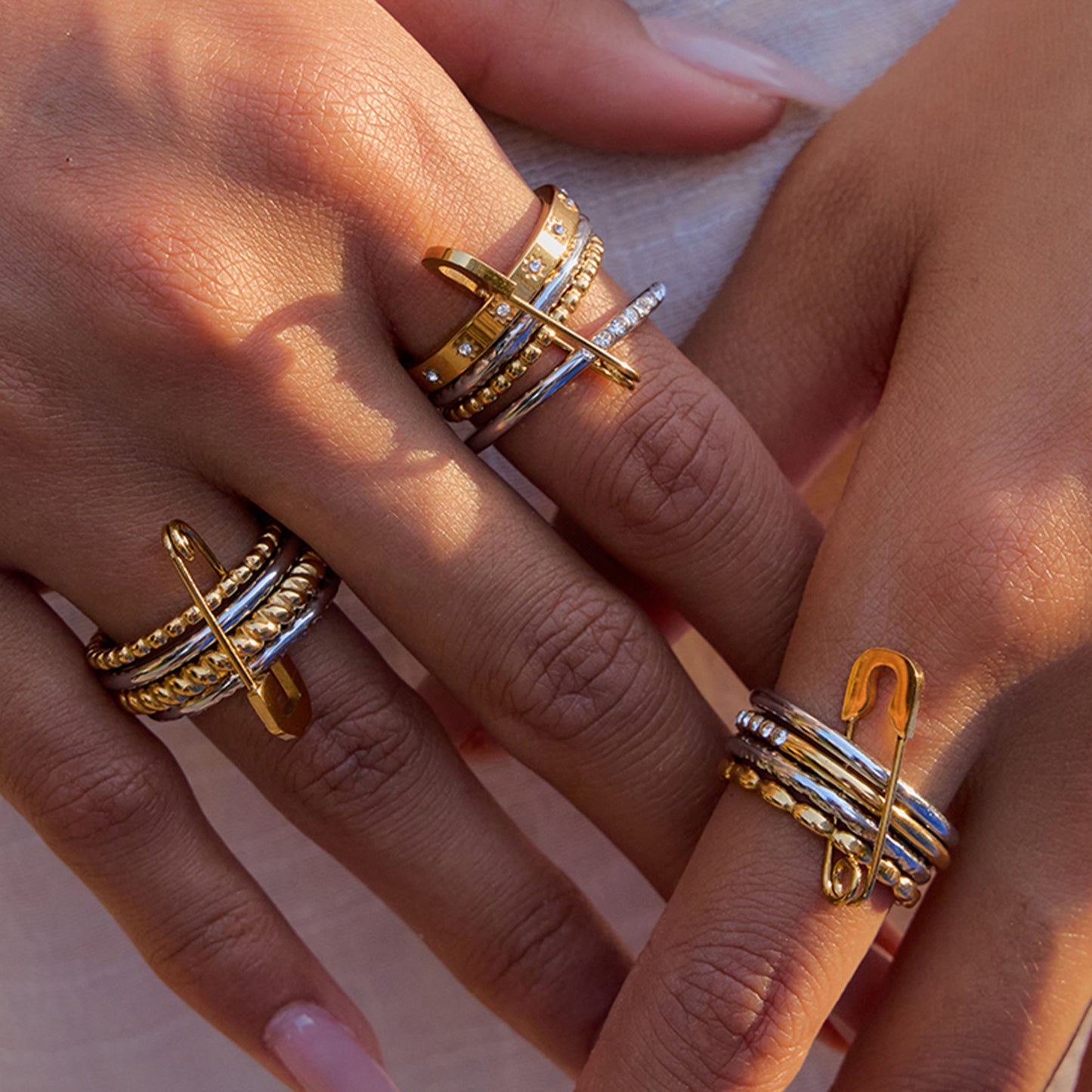 Close-up of hands wearing multiple gold and silver rings on a light background