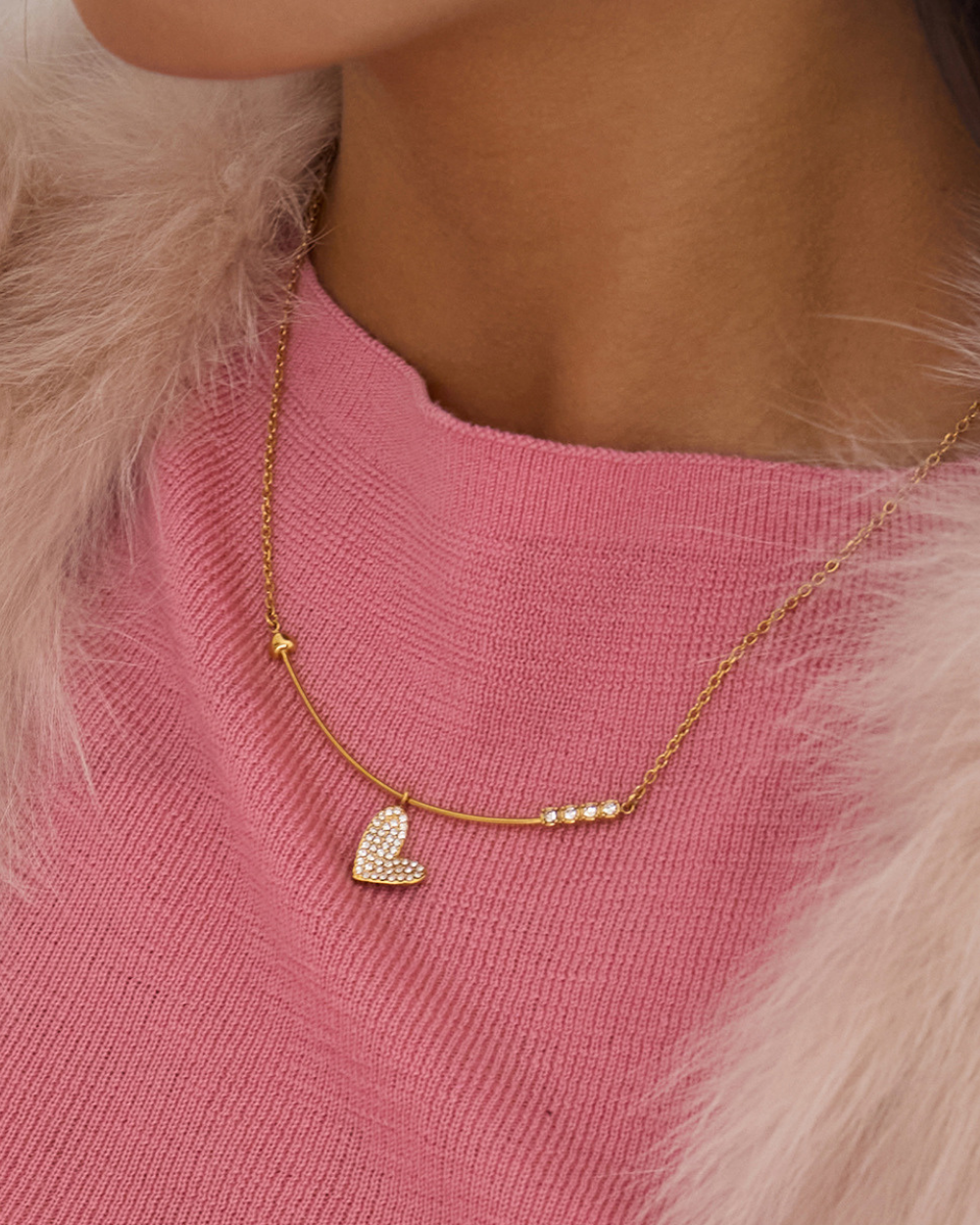 Gold necklace with a heart pendant on a pink sweater
