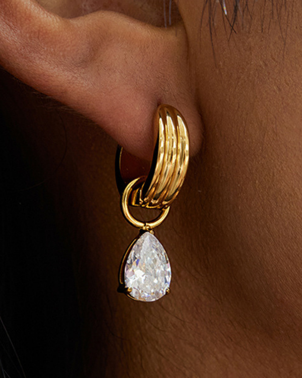 Gold hoop earring with a teardrop-shaped gemstone worn on an ear.